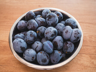 Metal bowl filled with ripe Prunus domestica plums on wooden surface. Natural source of fiber, antioxidants and vitamins, supports digestion and immune system.