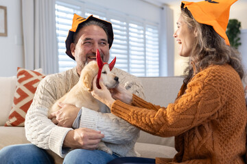 Couple styling puppy with red devil-horn headband on sofa while wearing Halloween bucket hats
