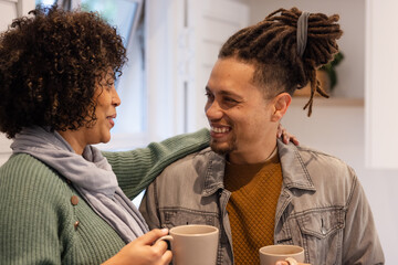 African American couple standing in modern kitchen sharing coffee mugs by potted plant