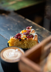 A slice of cake served with a cup of cappuccino featuring latte art, placed on a rustic wooden...