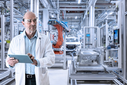 Manager in lab coat supervising modern factory with tablet