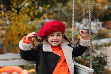Happy beautiful baby girl in red beret in autumn park riding on swing. autumn concept. autumn mood. fall