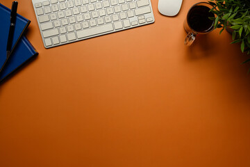 Stylish workspace with white keyboard, coffee cup, and green plant on orange background