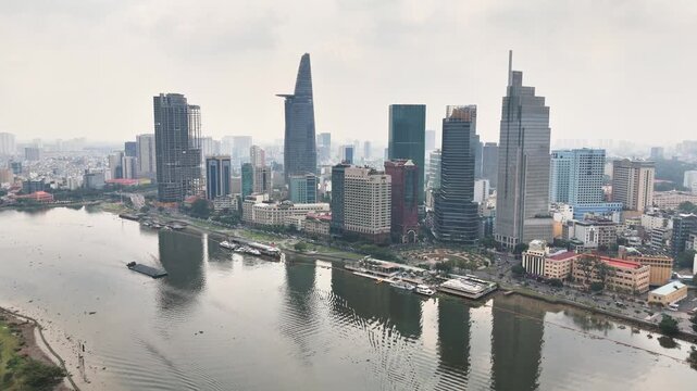 Drone view over central Ho Chi Minh City, Vietnam, featuring the Saigon River and iconic skyline with Bitexco Financial Tower and Landmark 81 reflecting in the water under bright daylight.