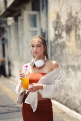 A beautiful teenage model girl posing on the streets of old town during street style photo shooting drinking ice fruit beverage