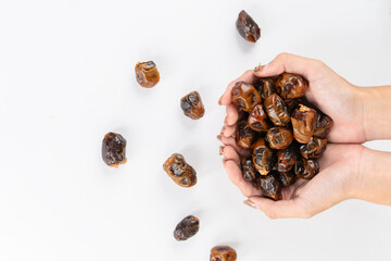 Obraz premium A pair of hands gently holding a bunch of dried dates over a clean white surface, with scattered dates adding a rustic and natural touch.