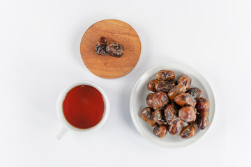 A bowl of dates and a cup of tea placed side by side on a white table for a serene snack moment, shot in soft natural light with a clean minimal look.