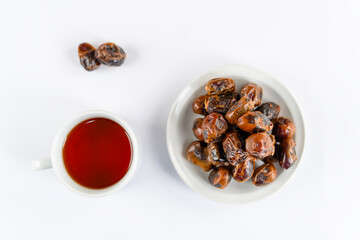 A bowl of dates and a cup of tea placed side by side on a white table for a serene snack moment, shot in soft natural light with a clean minimal look.