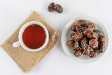 A bowl of dates and a cup of tea placed side by side on a white table for a serene snack moment, shot in soft natural light with a clean minimal look.