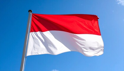 The red and white national flag of Indonesia waving gently in the wind against a bright blue sky.