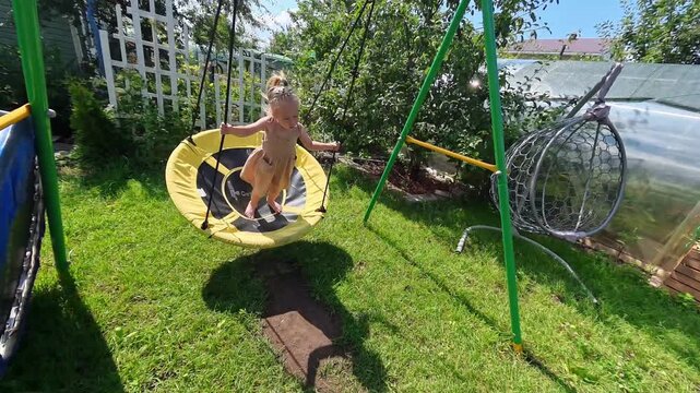 A little child girl in a dress swings on a big round swing in summer. Shot on an action camera. amara, Russia - 10 July 2025