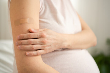 Close-up shot of fresh vaccination plaster on expecting mother's arm. Crucial maternal and fetal...