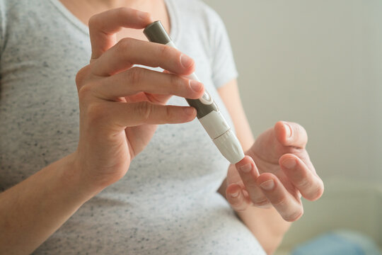 Close-up of pregnant female using glucometer to measure blood sugar levels. Vital health check for preventing gestational diabetes complications.