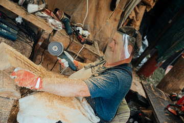 A focused craftsman uses a power tool to carve wood, surrounded by sawdust and tools, wearing full protective gear in a busy workshop