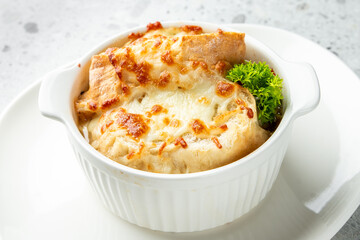 Baked appetizer in white ramekin with melted cheese, toasted bread, and parsley garnish, served on white plate. Close-up shot with light background.