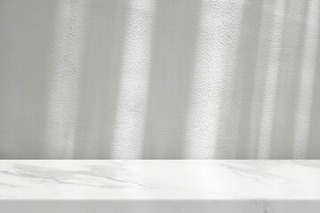 White marble table with a white stucco wall texture background featuring natural light beams and shadows