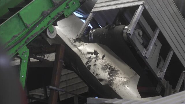 Crushed rubber chunks fall into metallic chute. Vibration carries scraps toward processing unit. Constant movement toward processing end