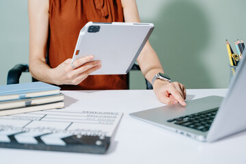 Creative female filmmaker working with tablet, clapperboard, and laptop in modern studio office. Film production, planning, and content creation scene.