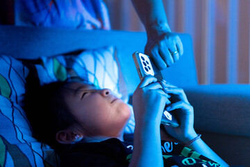 Parent taking smartphone from child at night in bed, concept of screen time limits, digital detox, and bedtime struggle