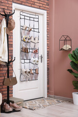 Organizer with different footwear on door, clothes and houseplant indoors. Shoe storage
