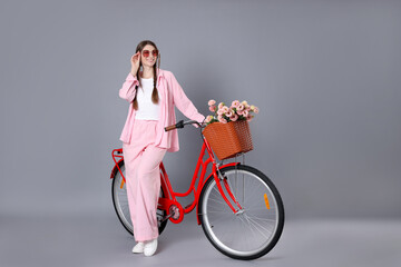 Smiling woman in sunglasses and bicycle with basket of flowers against grey background