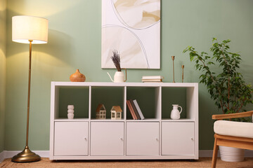 Shelving unit with decorative elements, lamp and houseplant near green wall indoors