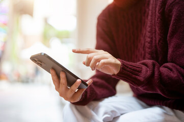 Close up of a hand holding and fingers hovering over smartphone while sitting in a building.