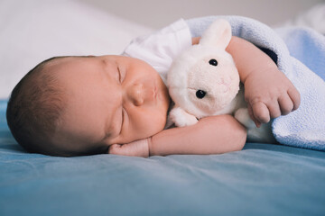 Newborn sleep at first days of life. Portrait of new born baby one week old with cute soft toy in crib in cloth background.