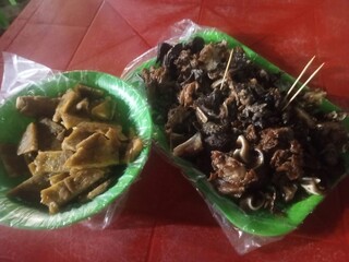 Gekochte Fleischstücke und Innereien auf grünen Plastiktellern serviert, traditionelle Straßengerichte mit Spießen und Beilagen.. Kolumbien