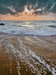 Ocean waves crashing on sandy beach at sunrise with dramatic sky