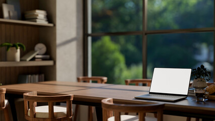 Blank screen laptop with bread and coffee on wooden table in a glass wall dining room or living room