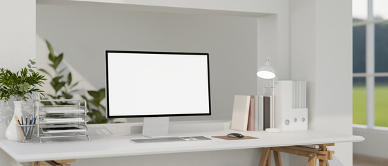 White screen computer with stationary and lamp on white table in a bright living room or office.
