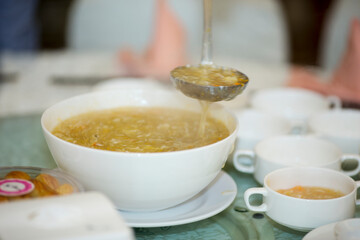 A ladleful of warm, savory soup with delicate strands, being served from a white bowl. A warm and elegant bowl of creamy asparagus soup, perfect as a comforting appetizer or light meal.
