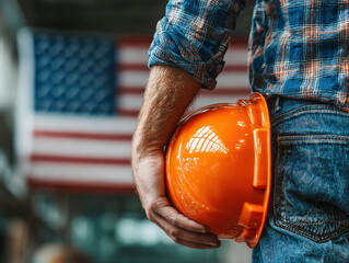 Construction worker holding orange safety helmet with american flag in background, celebrating labor day