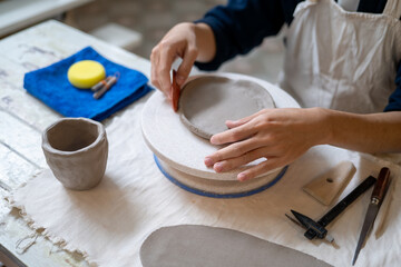 Close up of potter artist scraping on clay to make a plate on working table in pottery class or studio.