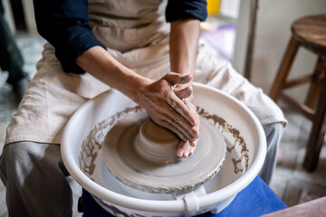 Close up of potter artist hands shaping clay into bowl on spinning throwing wheel in class or studio