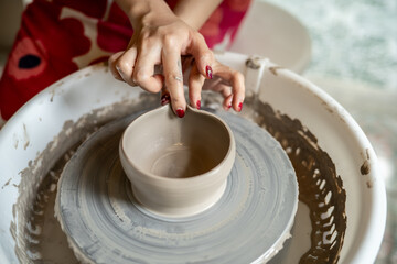 Pottery artist hand molding clay into tea brewing bowl on spinning throwing wheel in class or studio
