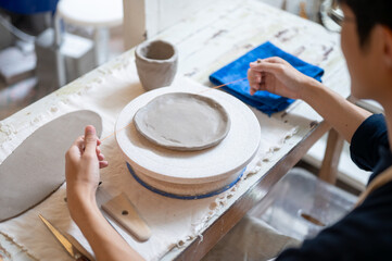 Pottery artist using wire cutter on clay slab on throwing wheel at working table in class or studio