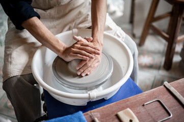 Top view of pottery artist's hands holding and molding a clay on throwing wheel in a class or studio