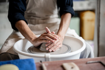 Close up of pottery artist's hands holding and molding a clay on throwing wheel in a class or studio