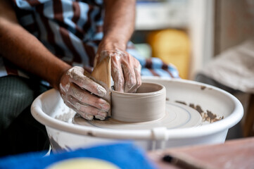 Close up pottery artist's hand using tool to smooth a clay bowl on throwing wheel in class or studio