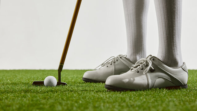 Close-up of golf shoes and putter on green grass. Concept of fashion and sportswear, wellness habits, and editorial publishing focused on female-focused active lifestyle.