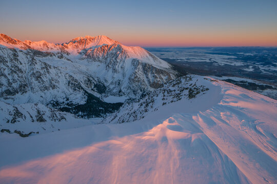 View of snow-capped peaks bathed in the warm glow of sunrise, contrasting with the cool blue sky, in Strbske Pleso, Pre&Aring;&iexcl;ov Region, Slovakia.