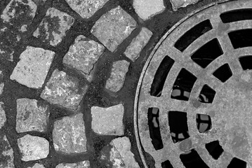 Manhole cover on a cobblestone road. View from above