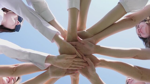 Group of friends enjoying a friendly meeting outdoors, with hands joined together in a circle under a clear blue sky, emphasizing teamwork and connection while sharing ideas over coffee and lunch.