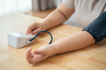 An Asian woman uses a portable blood pressure monitor in her living room. Health awareness concept.