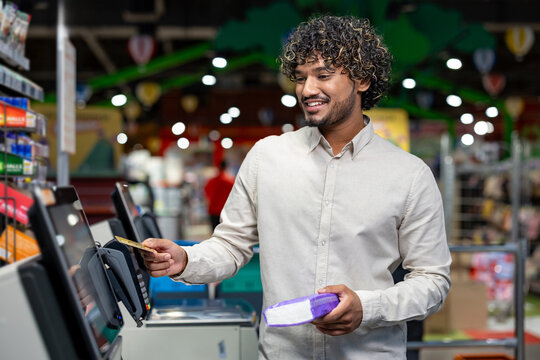 A smiling man pays for groceries with a credit card at the self-checkout in a supermarket.