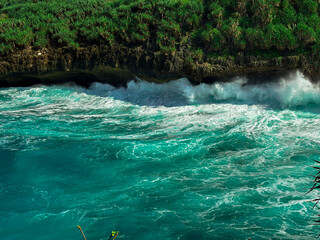 Naklejka premium Turquoise Sea Waves: Captivating turquoise waves crash against the rugged coastline. Lush greenery frames the stunning view, showcasing the raw power and beauty of the ocean. 