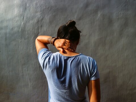 Asian Indonesian woman with stain on t-shirt sweat patch under back against gray background. Need deodorant. Uncomfort after exercise or hard activity