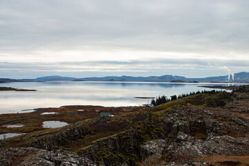 Naklejka premium Autumn mountain landscape with a scenic lake reflecting the forest and cloudy sky in Nordic landscape, Iceland